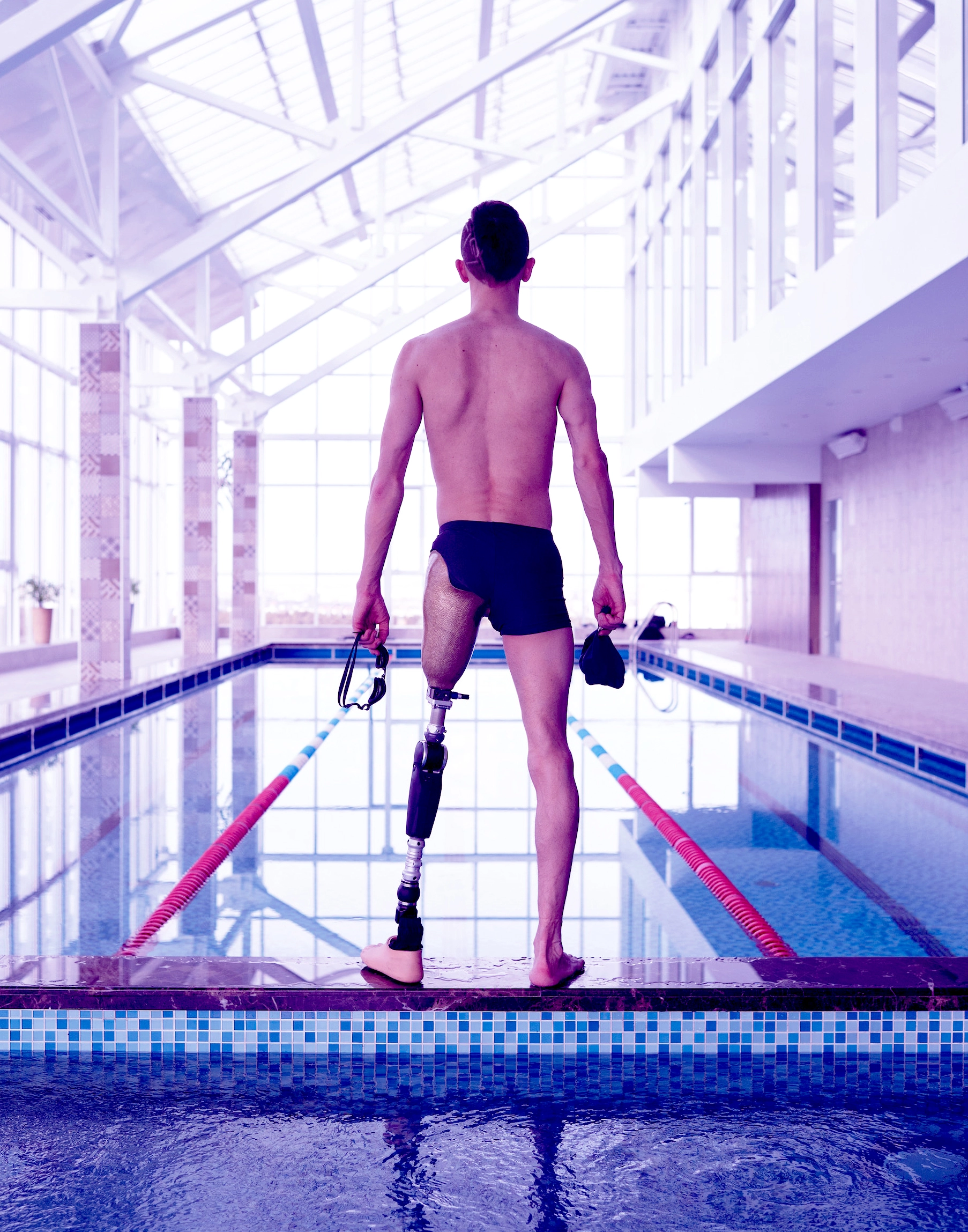 Person with a leg prosthetic standing in front of a swimming pool, their back towards the camera